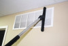 A sidewinder attached to a wand cleaning a vent high up on a wall.
