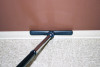 A sidewinder tool on a wand cleaning the top edge of a baseboard.