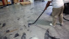 Person cleaning concrete floor with S-wand and floor brush.