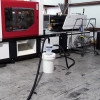 12 gallon separator bucket with hoses attached sitting in front of a molding machine.