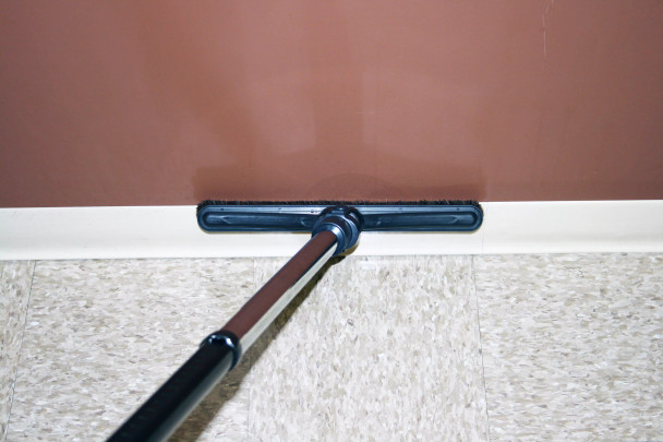 A sidewinder tool on a wand cleaning the top edge of a baseboard.