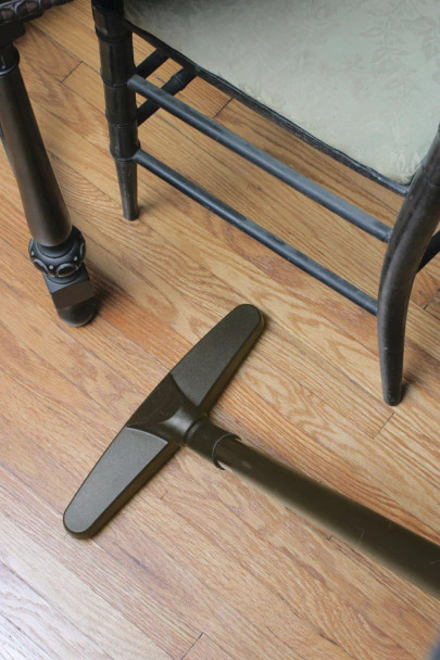 A floor brush on a wand cleaning under a chair.