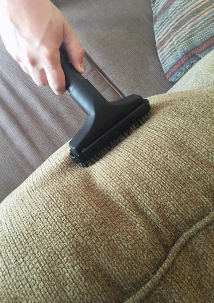 Person vacuuming couch with upholstery tool with slide-on brush.