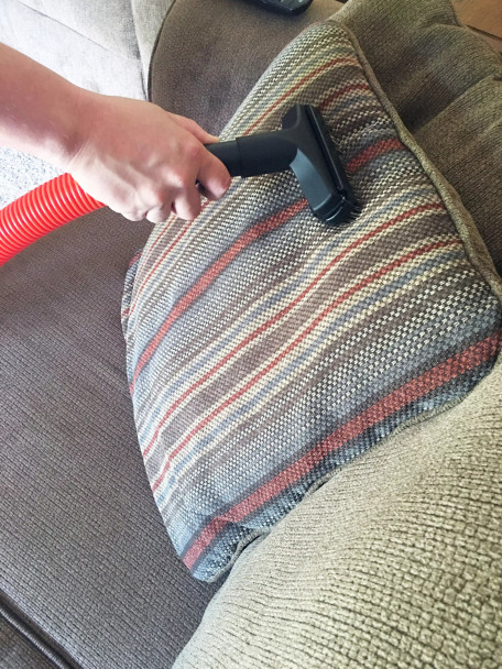Person vacuuming pillow on couch with upholstery tool with slide-on brush.