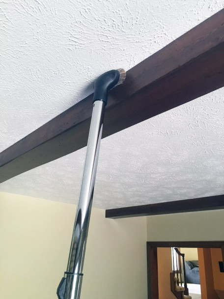 Dust brush attached to chrome wand cleaning a rafter.
