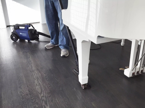 Person using Sidewinder connected to the C105 vacuum to clean under a piano.