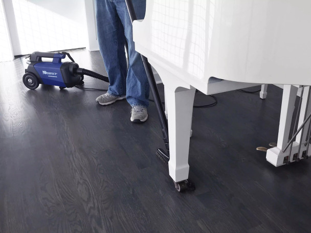 Person using Sidewinder to vacuum hard floor around a piano.