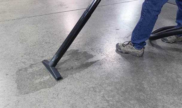 Person using squeegee floor brush to clean up a spill on a concrete floor.