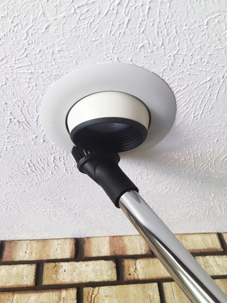 Dust brush attached to chrome wand cleaning inset light on ceiling.