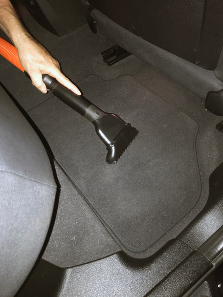 Upholstery tool cleaning the floor rug in a car.