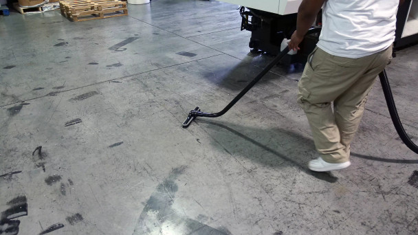 Person cleaning concrete floor with S-wand and floor brush.