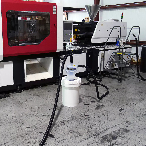 12 gallon separator bucket with hoses attached sitting in front of a molding machine.