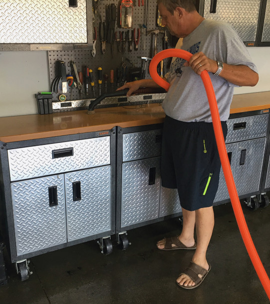 Someone holding the orange hose and vacuuming their counter space in their garage.
