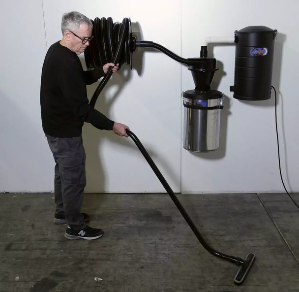 Person cleaning floor with floor brush and S-wand connected to a hose reel, separator and vacuum hanging on a wall.