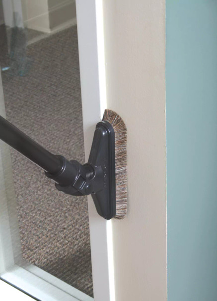 A sidewinder brush attached to a ratcheting wand cleaning a door frame. The wand has the brush low on the frame with the swivel neck at a 45 degree angle.
