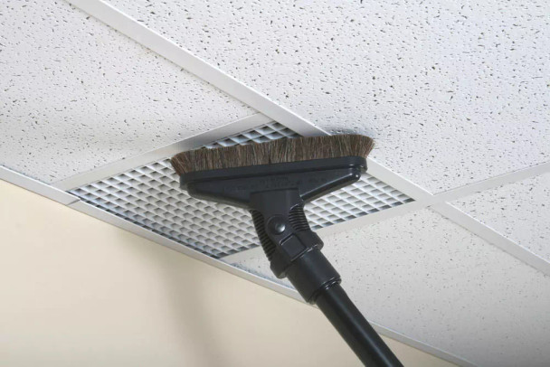 A sidewinder brush attached to a wand cleaning a ceiling tile.