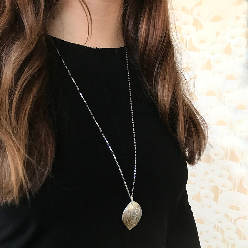Model shot. Luxurious fine silver with fine 24ct gold pendant.
Handcrafted using the age old Korean technique of Keum Boo, where 24ct gold is fused to the surface of the silver.
The metal is then embossed with specialised templates to create the desired layering of grass and Hakea nut imagery. 


 