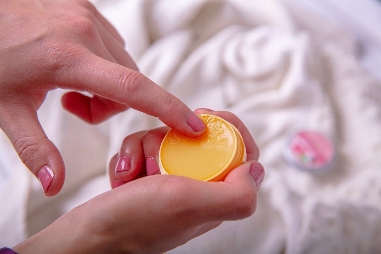 A woman holds a topical balm in one hand and touches it with the other.