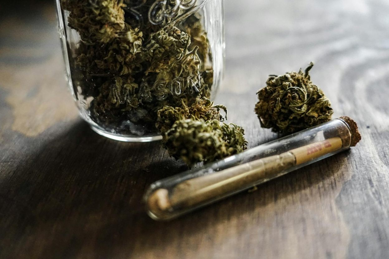 Two cannabis buds and a joint next to a cannabis jar