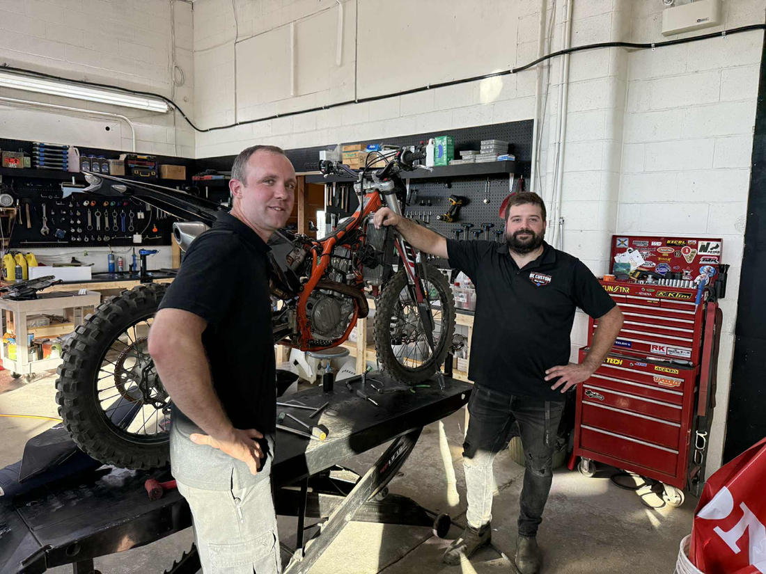 Two True Tech technicians posing with a dirt bike on the lift