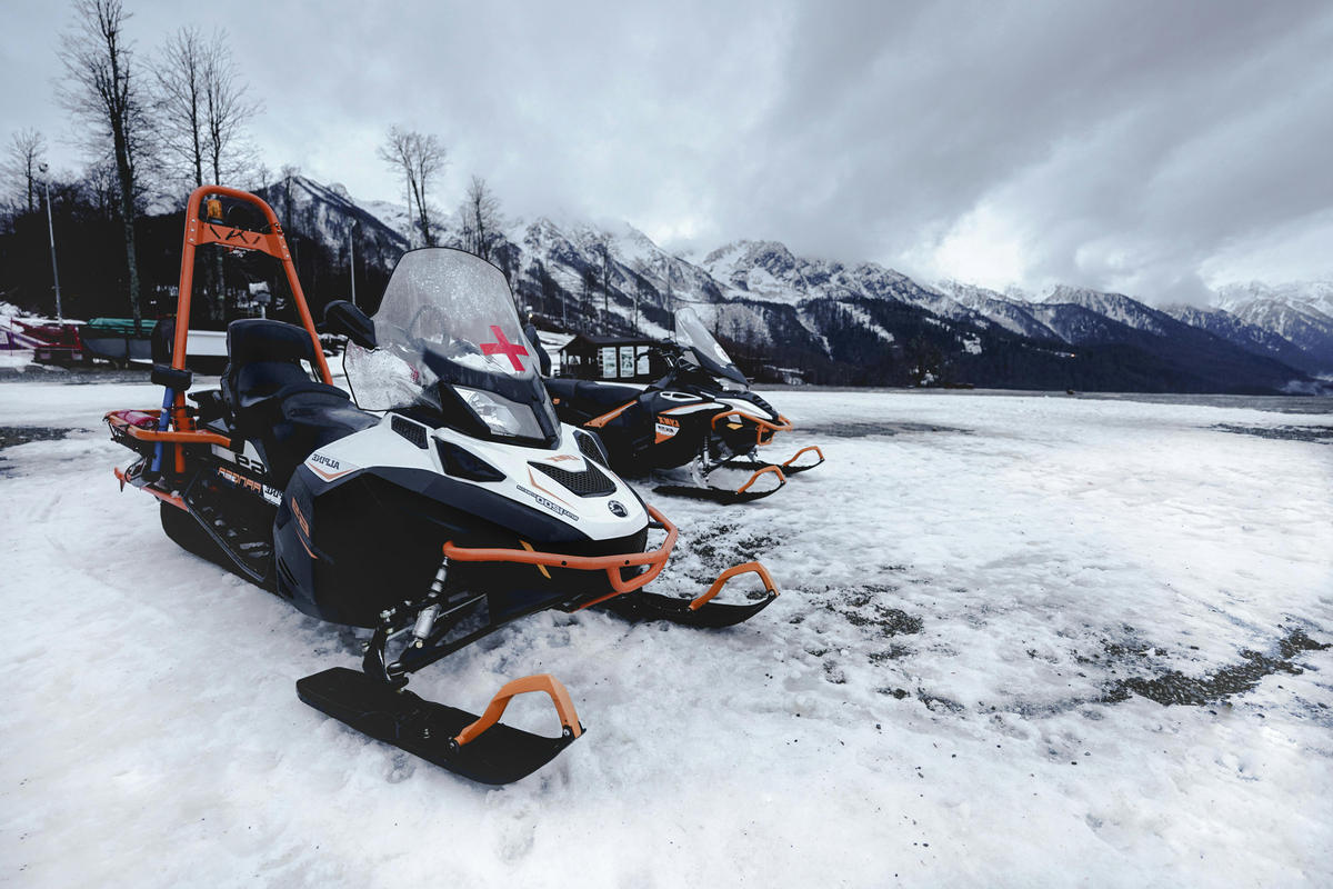 Two snowmobiles parked on snow with mountains behind