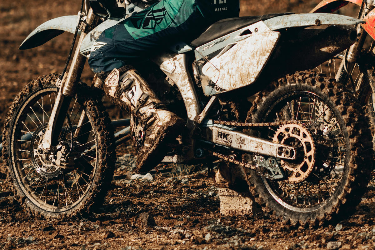 Mud-covered dirt bike wheel, chain and rider's boot, close up