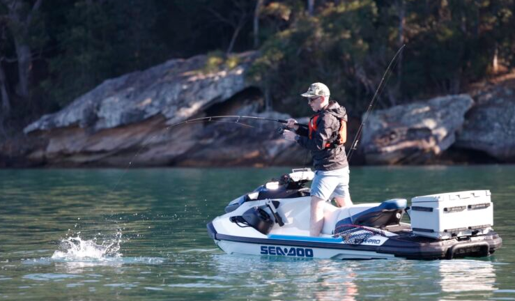 Rider standing on a Sea-Doo personal watercraft, fishing on calm water