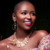 Iboju hoop african mask inspired earrings on african american model smiling with short hair in gold necklace with floral dress against a black background