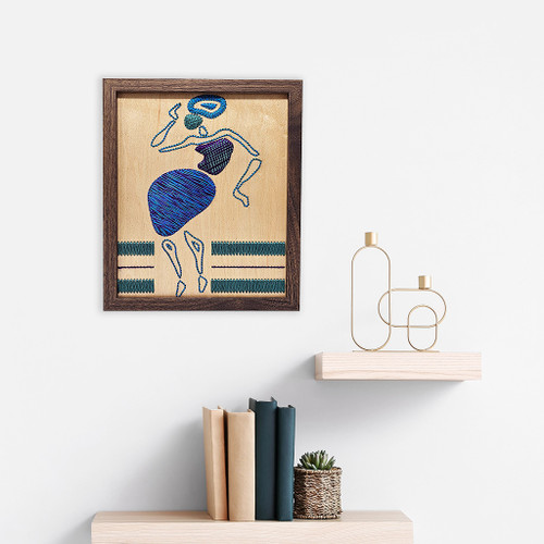 embroidery in wood home decor piece Ijo ayo blue purple green embroidery in wood above wooden shelf with books and gold decor by artist atinuke adeleke for zuri perle  embroidery in wood home decor piece Ijo ayo blue purple green embroidery in wood above wooden shelf with books and gold decor by artist atinuke adeleke for zuri perle