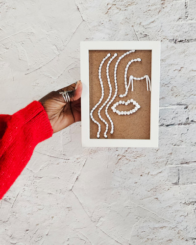 hand embroidery on wood line portrait of woman home decor piece white embroidery on brown wood against white textured wall contemporary African art by Dallas brand Zuri Perle