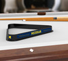 Michigan Wolverines billiard triangle displayed on a pool table beneath billiard cues, showcasing the black frame, maize and blue Michigan graphics, and Block M logo in a game room setting.