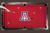 Arizona Wildcats red logo billiard cloth shown installed on a full-size pool table during play. The red playing surface features a large Arizona Wildcats block A logo at center with billiard balls positioned across the table and a player preparing to take a shot.
