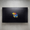 Kansas Jayhawks pool table cover shown from above, featuring a black cover design with the colorful Kansas Jayhawks logo centered on the surface. This NCAA billiard table cover is designed to protect the table while showcasing University of Kansas team pride.