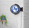 Lifestyle view of the Air Force Academy Falcons Original Round Rotating Lighted Wall Sign mounted on a white brick wall, demonstrating its appearance as game room, home bar, or fan cave decor.