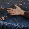 Close-up view of the black woven leaf-net material with leaves resting on the surface, highlighting the fine mesh construction designed to catch leaves and debris while allowing water to pass through.