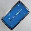 Overhead lifestyle view of the Wisconsin Badgers Team Color Laser Etched Cue displayed diagonally across a blue-felt pool table, showcasing the collegiate billiard cue in a home game-room setting.