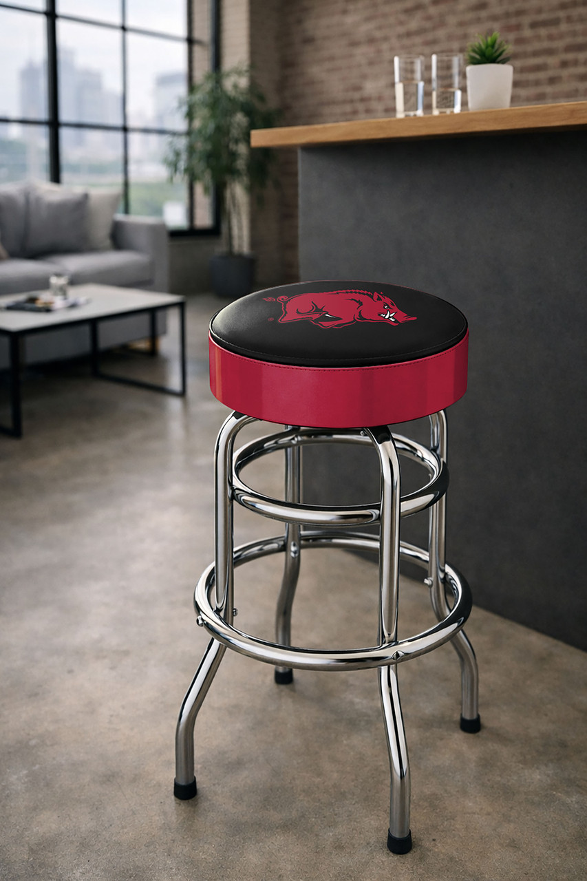 Arkansas Razorbacks 30" chrome bar stool displayed in a home entertainment setting, featuring a cardinal red and black team logo seat with a polished chrome base. This college team stool is perfect for adding Arkansas spirit to a fan cave, home bar, pool room, or game room.