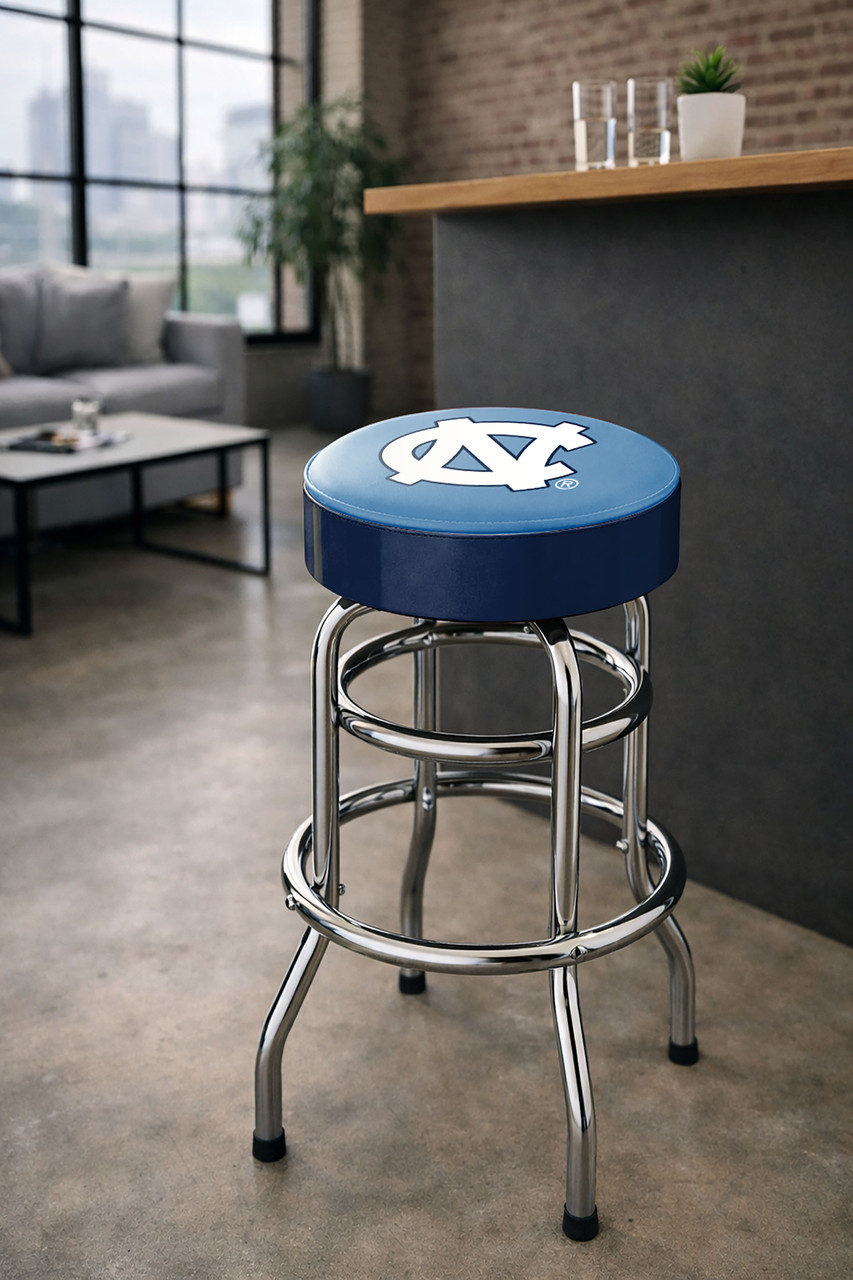 North Carolina Tar Heels 30" chrome bar stool displayed in a home entertainment setting, featuring a Carolina blue and white team logo seat with a polished chrome base. This college team stool is perfect for adding UNC spirit to a fan cave, home bar, pool room, or game room.