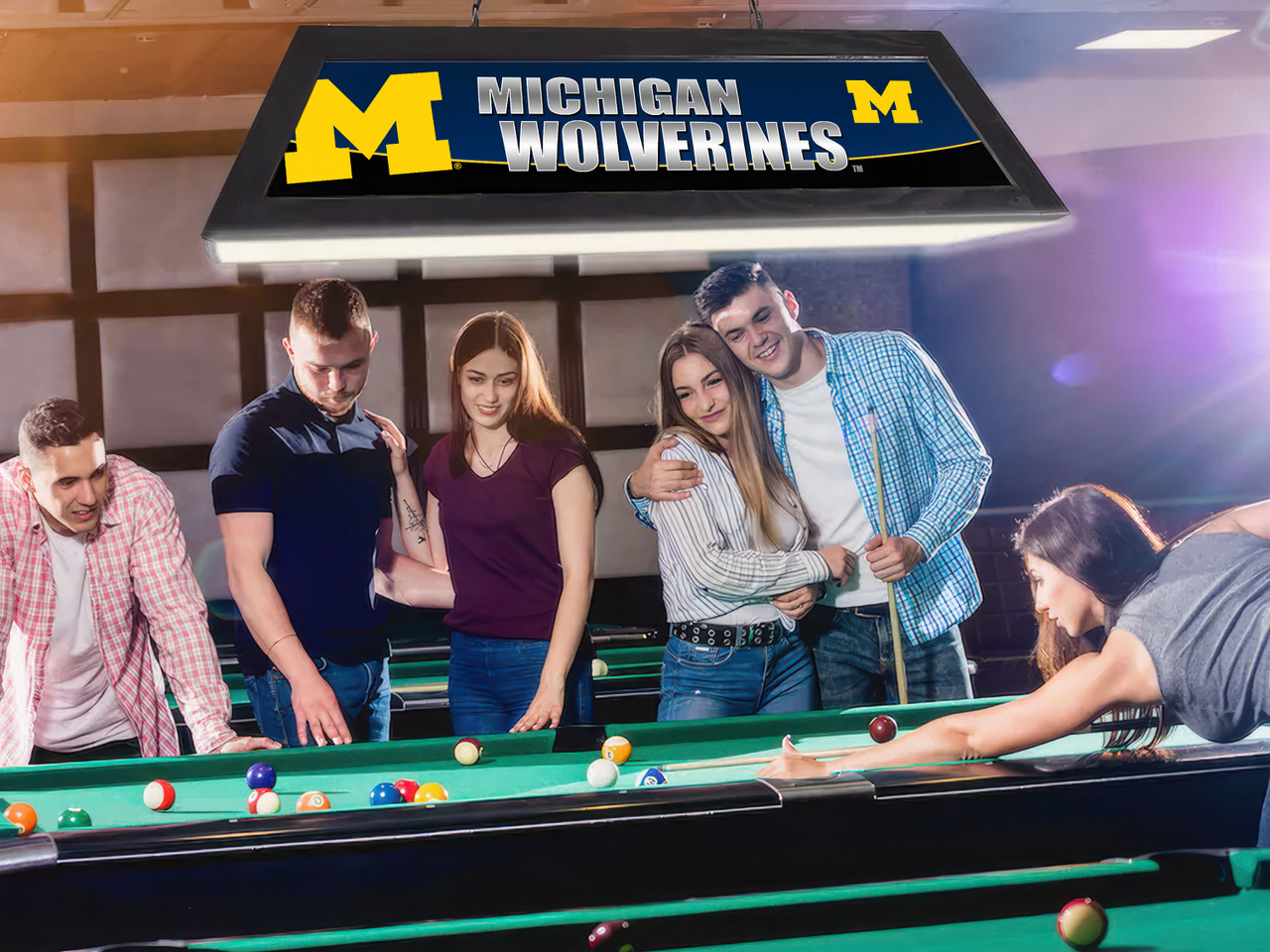 Lifestyle view of the Michigan Wolverines 42-inch hanging billiard table light installed above a pool table, demonstrating its appearance in a game room, billiard room, home bar, or Wolverines fan cave.