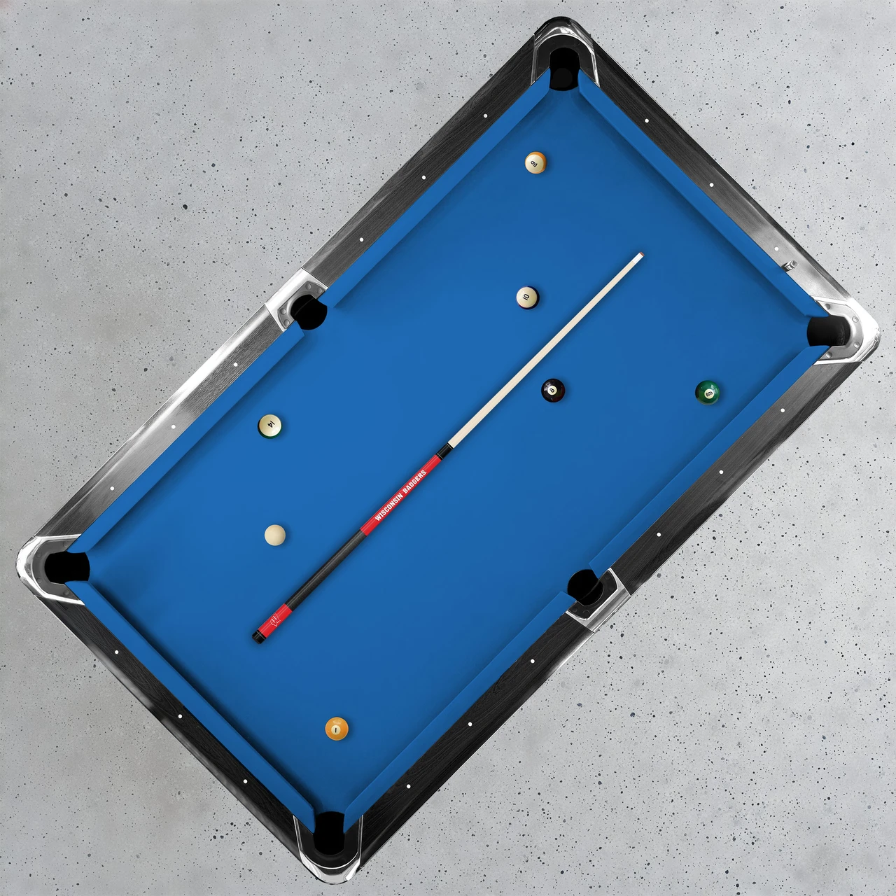 Overhead lifestyle view of the Wisconsin Badgers Team Color Laser Etched Cue displayed diagonally across a blue-felt pool table, showcasing the collegiate billiard cue in a home game-room setting.