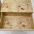Open wooden drawer with a smooth, natural burl wood pattern. The grain and knots create a unique, textured appearance on the light beige surface.