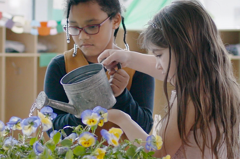 two young students watering a flower garden