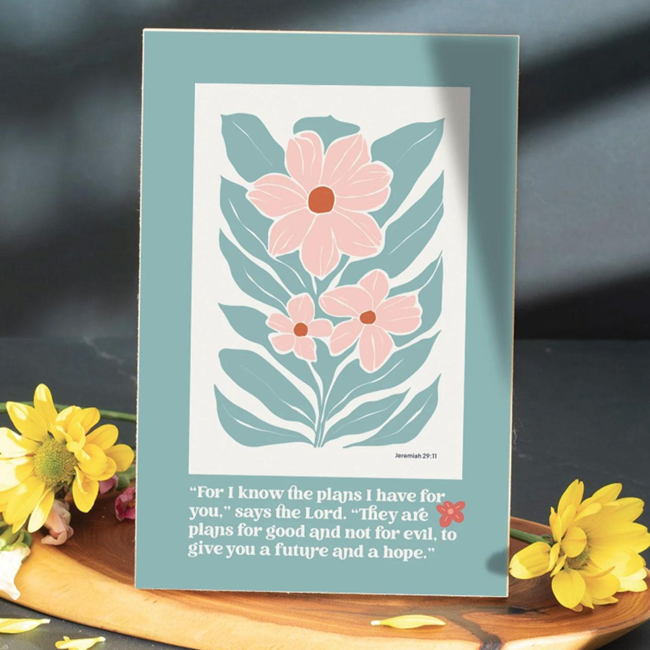 The For I Know The Plans Wall Plaque shown on a table with yellow flowers