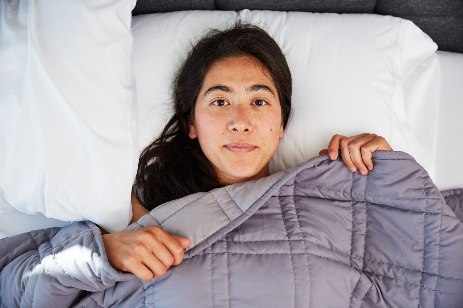 Woman awake in bed under Moonbow Cooling Weighted Blanket