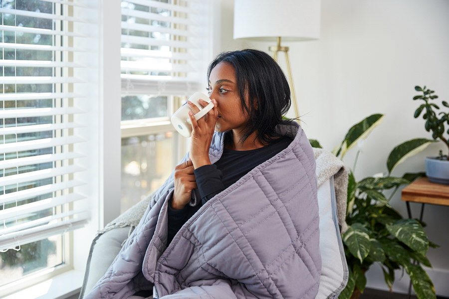 Woman drinking coffee while wearing Moonbow Cooling Weighted Blanket