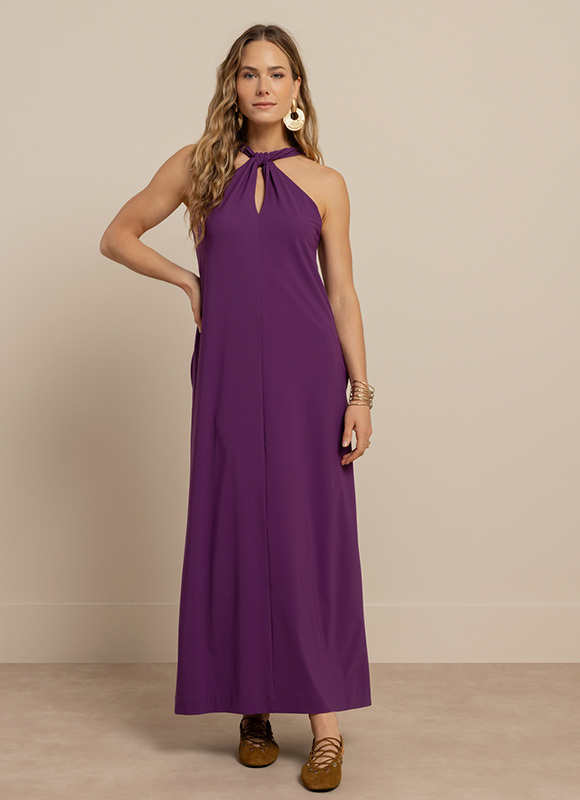 Vrouw draagt een lichtblauwe jumpsuit met lange mouwen en een strikdetail bij de hals, gecombineerd met hakken. De look laat een elegante en moderne optie zien voor zowel werk als gelegenheid.