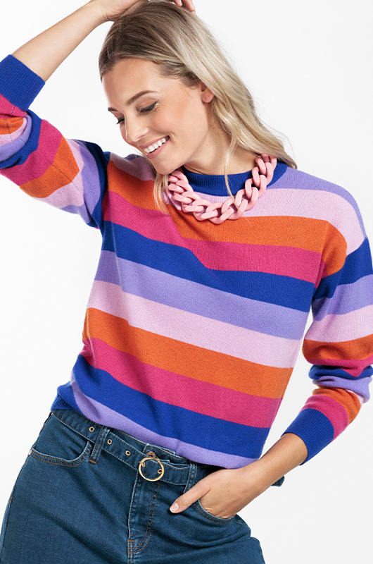 Blond model dat schuin naar beneden kijkt met een streepjes trui aan in de kleuren oranje, roze, blauw, paars en oudroze