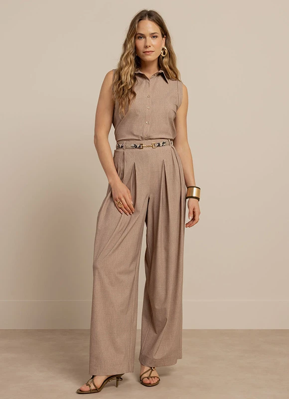 Vrouw draagt een pak met een drukke print en een feloranje top en staat rechtop tegen een neutrale achtergrond. De combinatie van kleur en patroon geeft de outfit een gedurfde en energieke uitstraling.