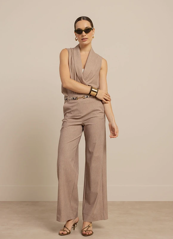 Vrouw draagt een lange jurk met grafische print in groen- en bruintinten en staat ontspannen met haar hand in haar zij. De vloeiende stof en opvallende print zorgen voor een elegante en expressieve look.