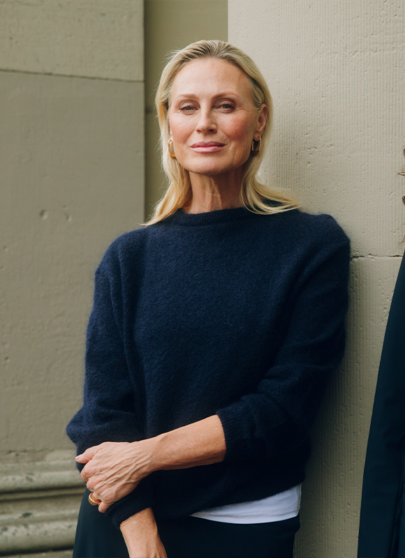 Vrouw draagt een donkerblauwe outfit met een mouwloze top en korte broek en staat ontspannen tegen een neutrale achtergrond. De sportieve sneakers en strakke lijnen geven de look een moderne en casual uitstraling.